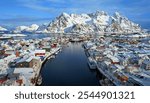 Picturesque snowy village along a fjord with colorful houses, framed by towering snow-capped mountains under a bright blue sky.