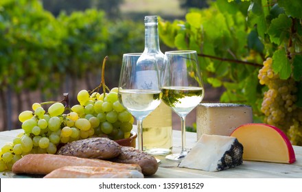 Picturesque still life – white wine, grapes and cheese against vineyard landscape - Powered by Shutterstock