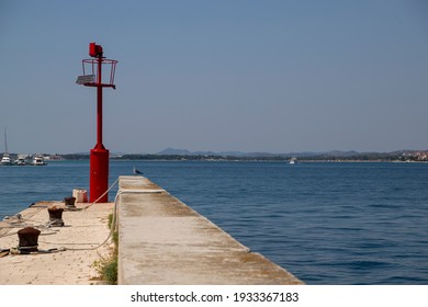 Picturesque Stone Peer With Red Steel Signal Post That Aids Safe Navigation Trough Shallow Waters And Easy Access To Krapanj Harbour On A Sunny Summer Day