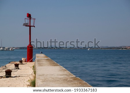 Picturesque stone peer with red steel signal post that aids safe navigation trough shallow waters and easy access to Krapanj harbour on a sunny summer day