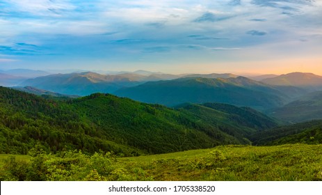 Picturesque sunset in the mountains. A calm evening fell on mountain ranges overgrown with green forest. The sky is painted with the warm colors of the setting sun