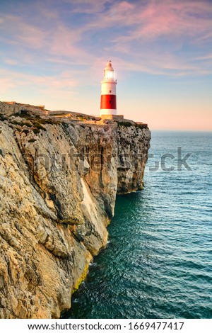 A picturesque sunset over Gibraltar's famous Trinity lighthouse, illuminating the rocky coast and guiding ships with its beacon.