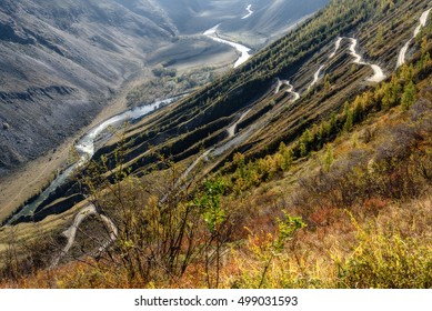 The picturesque top view on the steep winding gravel road through the pass, going up the mountain slope, the valley between the mountains and the river 