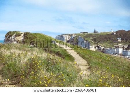 A picturesque trekking trail meanders through the lush grasslands atop a stunning sea cliff in Étretat