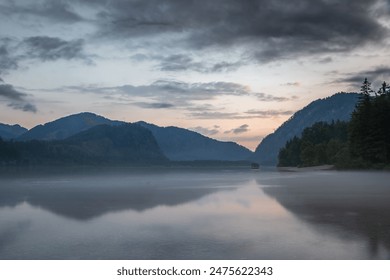 A picturesque view of Almsee Lake with a small wooden hut in Austria at sunset. The sky is filled with beautiful, colorful clouds, and the mountains in the distance are reflected in the calm water.  - Powered by Shutterstock