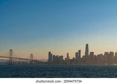 A picturesque view of The Bay Bridge and San Francisco Skyline Panorama at sunset golden hour from Treasure Island, California, United States. Cityscape with mist and foggy air.
