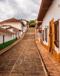A Picturesque View Of A Cobblestone Street In Barichara, Santander, Colombia, Lined With Traditional White Colonial Houses With Wooden Doors And Red Tile Roofs