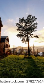 A picturesque view of a developing mountain town during golden hour, featuring modern architecture and lush green landscapes