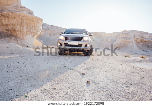 Picturesque view of dry rocky formations in canyon
with uneven sandstone mountains with jeep  parked under cloudless
blue sky