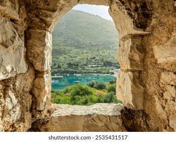 Picturesque view framed by stone window of watching tower of Porto Palermo fortress in Vlore, Albania. Vista reveals serene bay with turquoise Ionian sea surrounded by lush greenery and rolling hills - Powered by Shutterstock