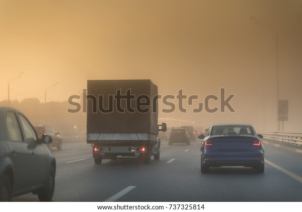 picturesque view of highway\
traffic in a sunny misty morning. Cars and small truck on the\
asphalt highway.
