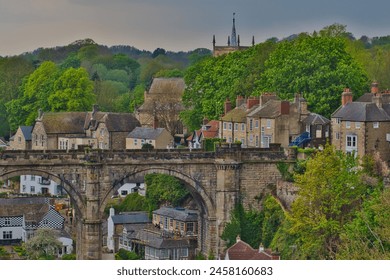 Picturesque view of a historic village with an old stone bridge, traditional houses, and lush greenery. - Powered by Shutterstock