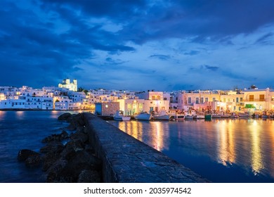 ギリシャの有名な観光名所パロス島にあるナウザ町の景色を眺めながら、夕方には伝統的な白塗りの家と係留漁船が照らされています