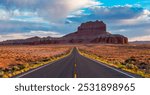 A picturesque view of an open highway stretching towards a striking red rock mountain under a vibrant sky in Utah. This scene captures the essence of adventure and natural beauty.