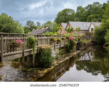 A picturesque view of a quaint village of Pontrieux in Brittany with stone houses, lush greenery, wooden bridge across Trieux river and a watermill Moulin du Richel. - Powered by Shutterstock