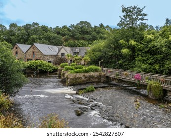 A picturesque view of a quaint village of Pontrieux in Brittany with stone houses, lush greenery, wooden bridge across Trieux river and a watermill Moulin du Richel. - Powered by Shutterstock