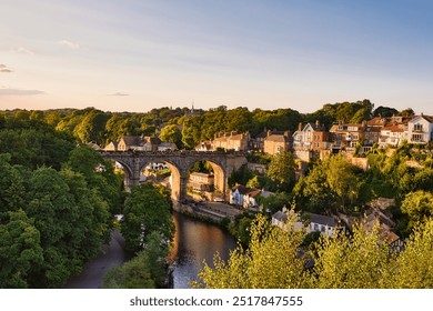 A picturesque view of a stone bridge arching over a river, surrounded by lush greenery and charming houses on the hillside. in Knaresborough - Powered by Shutterstock