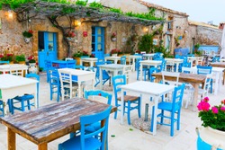 Picturesque Village Of Marzamemi, In The Province Of Syracuse, Sicily - Tables And Chairs Setup In Traditional Italian Restaurants In The Main Square Of The Historic Village During A Sunny Day