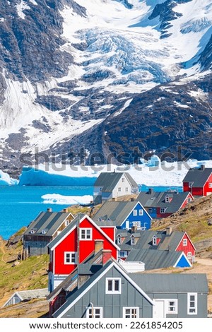 Picturesque village on coast of Greenland a giant iceberg in the background - Colorful houses in Tasiilaq, East Greenland