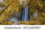 A picturesque waterfall flows through the heart of an autumn forest in Spearfish Canyon, South Dakota. Surrounded by vibrant fall foliage, the scene is a breathtaking display of nature