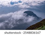 Picturesque winding path through a green grass field in hilly area in morning at dawn against blue sky with clouds. Natural panoramic spring summer landscape.