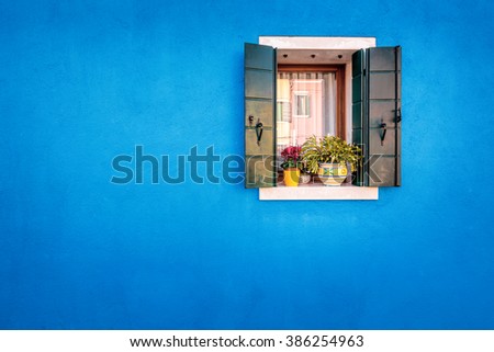 Picturesque window with blue house reflection on yellow wall of houses on the famous island Burano, Venice, Italy