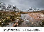 Picturesque winter landscape of Glen Coe with the iconic white cottage at the foot of  Buachaille Etive Mor, River Coupall and stormy clouds on the horizon.