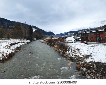 A picturesque winter village nestled by a flowing river, surrounded by snowy mountains. The cozy cabins and serene environment make it an ideal winter retreat, showcasing the beauty and tranquility of - Powered by Shutterstock