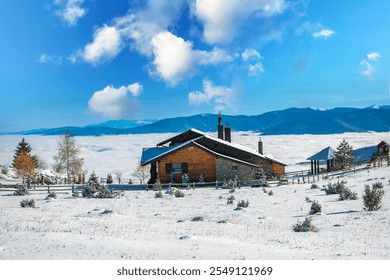 A picturesque wooden cabin surrounded by a snowy field, perched above a sea of clouds. The vibrant blue sky and scattered white clouds enhance the serene winter landscape - Powered by Shutterstock