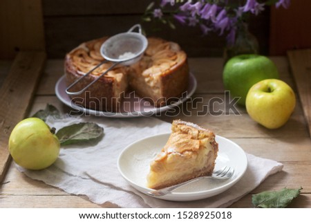 Pie with apple cream filling, apples and dishes on a wooden background. Rustic style.