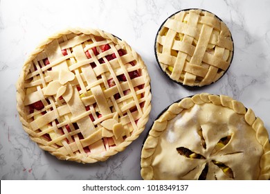 Pie Crust Design Ideas - Various Ways Of Pie Decoration With Lattice And Leaves. Apple, Strawberry And Raspberry Pies Uncooked On White Marble Table. 