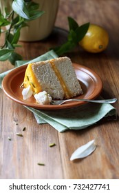 Piece Of Angel Food Cake With Lemon Curd Decorated With Pistachios And White Chocolate Leaves, On Brown Plate, On Wooden Table.