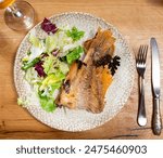 Piece of baked perch with side dish of fresh vegetables is served on plate. Fish is guaranteed with salad of lettuce and parsley, complemented by glass of beer.