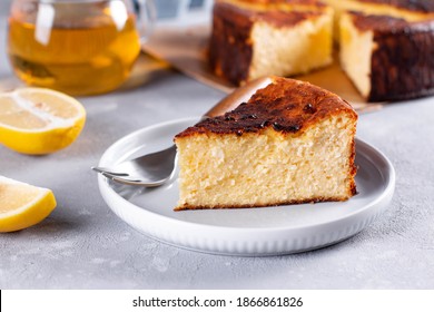 A Piece Of Basque Burnt Cheese Cake Put, The Whole Cake Is At The Background And Cup Is Also On The Table