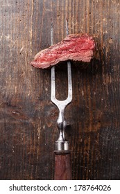 Piece Of Beef Steak On Meat Fork On Wooden Background