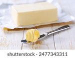 piece butter and knife on a white wooden table, selective focus. Close-up of butter curl