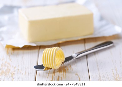 piece butter and knife on a white wooden table, selective focus. Close-up of butter curl