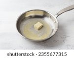 A piece of butter is melted in a frying pan on a light gray background. Making cheese pasta sauce, step by step, do it yourself, step 1