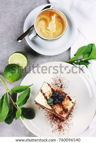 a piece of cake with a cup of cappuccino on the background of a slice of lime and twigs of mint.