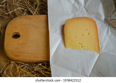 A piece of cheese on waxed wrapping paper. Wooden kitchen board and straw. Copy space. - Powered by Shutterstock