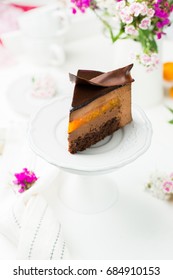 A Piece Of Chocolate Mousse Cake With Apricot On A Wooden White Background. Fresh Apricots And Bright Flowers