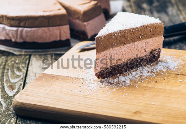 Piece of chocolate mousse cake sprinkled with\
coconut on the old wooden\
backround.