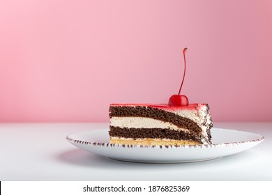 Piece Of Chocolate Vanilla Cake With Maraschino Cherry. Side View Cake On Pink Background