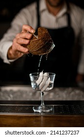 Piece Of Coconut In A Male Hand Over Cocktail Glass With Drink On The Bar Counter