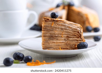 Piece of Crepes cake Suzette decorated with fresh blueberries and a   orange zest, sprinkled with powdered sugar on a white wooden table, selective focus.Concept of desserts for Shrove Tuesday. - Powered by Shutterstock