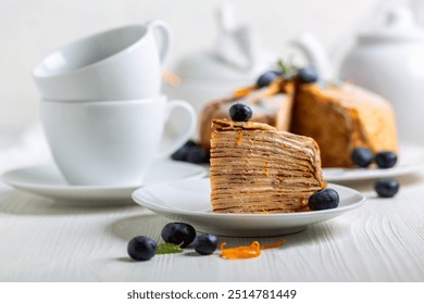 Piece of Crepes cake Suzette decorated with fresh blueberries and a orange zest, sprinkled with powdered sugar on a white wooden table, selective focus. Concept of desserts for Shrove Tuesday. - Powered by Shutterstock