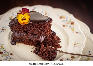 Piece of delicious rich chocolate cake decorated with a fresh pansy flower. Selective focus - Powered by Shutterstock