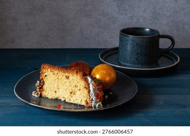 A piece of Easter cake and Easter eggs on a plate with a cup of tea on the table.