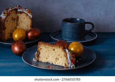 A piece of Easter cake and Easter eggs on a plate with a cup of tea on the table.