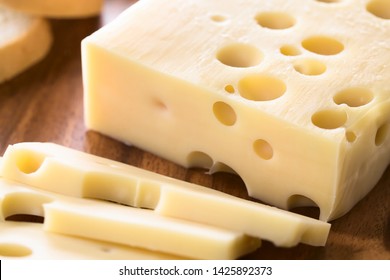 Piece of Emmental, Emmentaler or Emmenthal cheese on wooden plate (Selective Focus, Focus one third into the cheese piece)